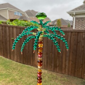 May include: A beaded palm tree decoration with a green crystal top and a colourful beaded trunk. The beads are in shades of brown, gold, and pink.