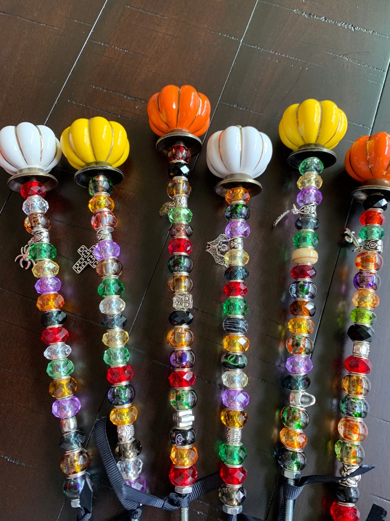 May include: Six decorative pumpkin-shaped garden stakes with colorful beads and charms. The pumpkins are white, yellow, and orange. The beads are red, green, purple, and clear. The charms include a spider, a cross, and a small metal charm.