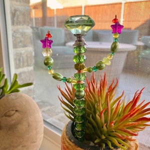 May include: A green beaded cactus with a large green crystal on top. The cactus is in a terracotta pot with a rope trim.