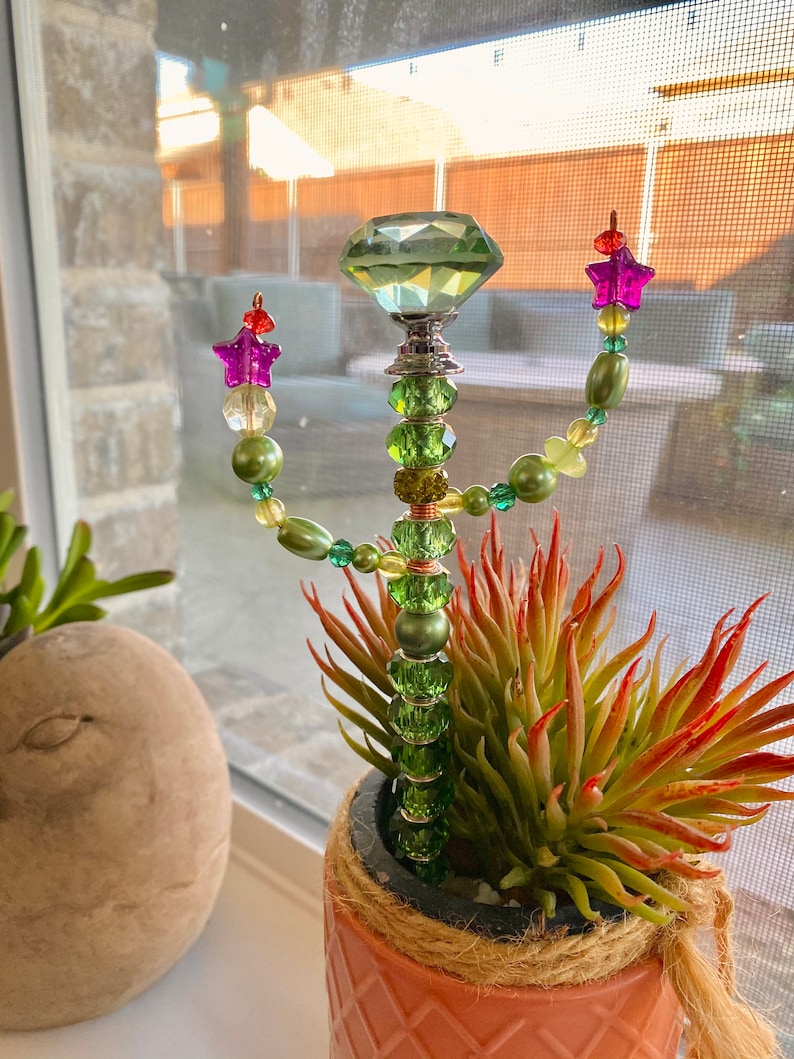 May include: A green beaded cactus with a large green crystal on top. The cactus is in a terracotta pot with a rope trim.