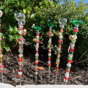 May include: Six decorative garden stakes with crystal and glass beads, bells, and charms. The stakes are adorned with red, green, and gold accents.
