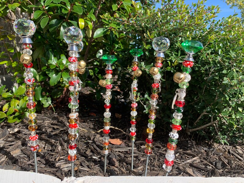 May include: Six decorative garden stakes with crystal and glass beads, bells, and charms. The stakes are adorned with red, green, and gold accents.