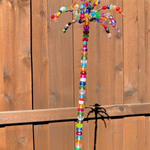 May include: A colourful beaded palm tree sculpture with a yellow top and a long string of beads in various colours, including red, green, blue, and purple.