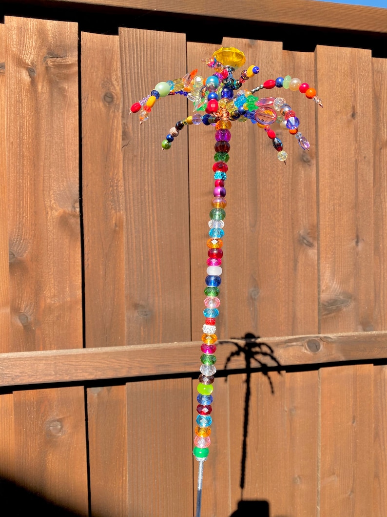 May include: A colourful beaded palm tree sculpture with a yellow top and a long string of beads in various colours, including red, green, blue, and purple.
