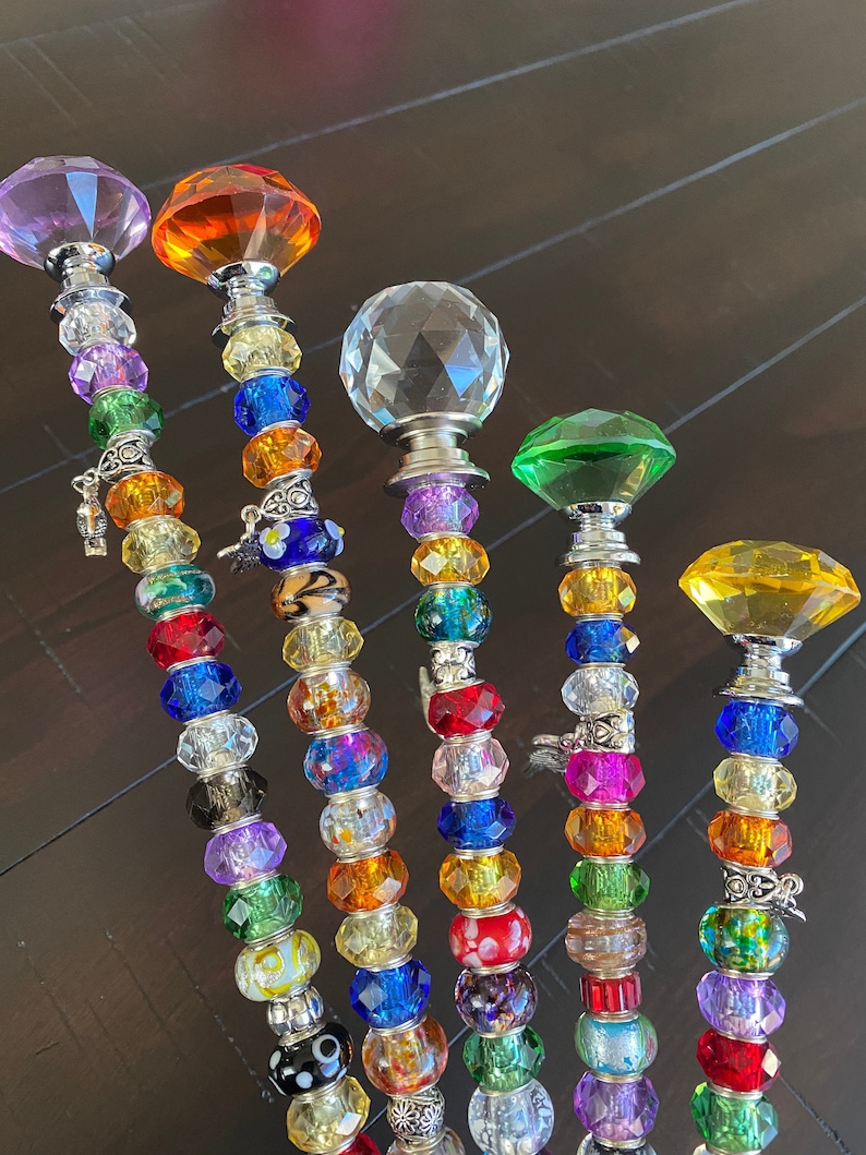 May include: Six colorful beaded wands with crystal tops. The wands are made with various colored beads and charms. The crystal tops are in shades of purple, orange, clear, green, and yellow.