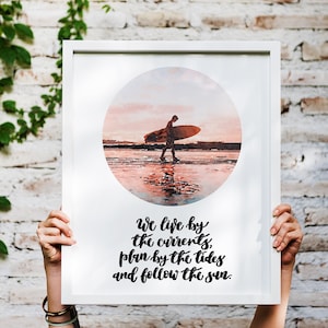 May include: A framed print with a watercolor illustration of a person surfing at sunset. The print has the text "We live by the currents, plan by the tides and follow the sun."