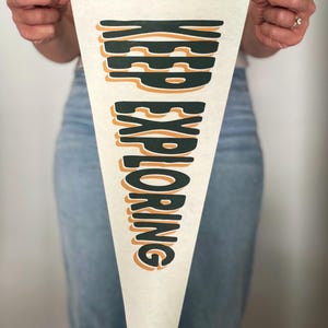 May include: A white pennant banner with green trim and the text "KEEP EXPLORING" in a retro, layered font with orange and green colors.