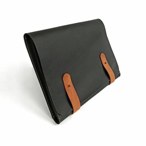 May include: A black leather portfolio with two brown leather straps and metal buckles.