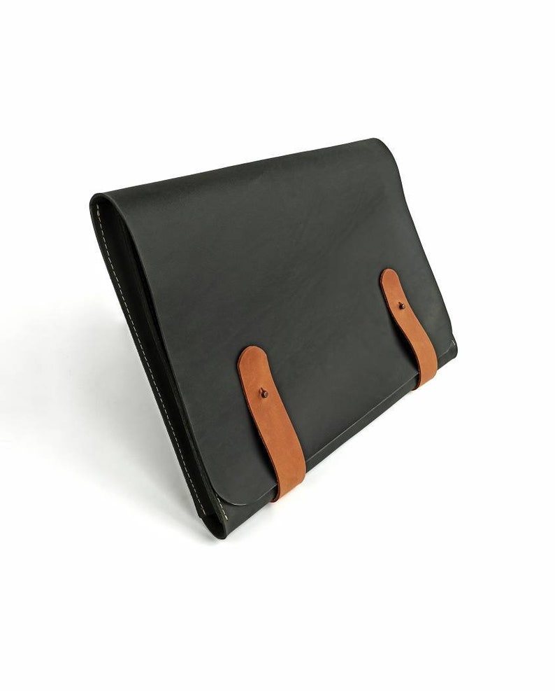 May include: A black leather portfolio with two brown leather straps and metal buckles.
