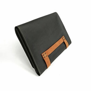 May include: A dark gray leather clutch with a brown leather strap and metal accents.