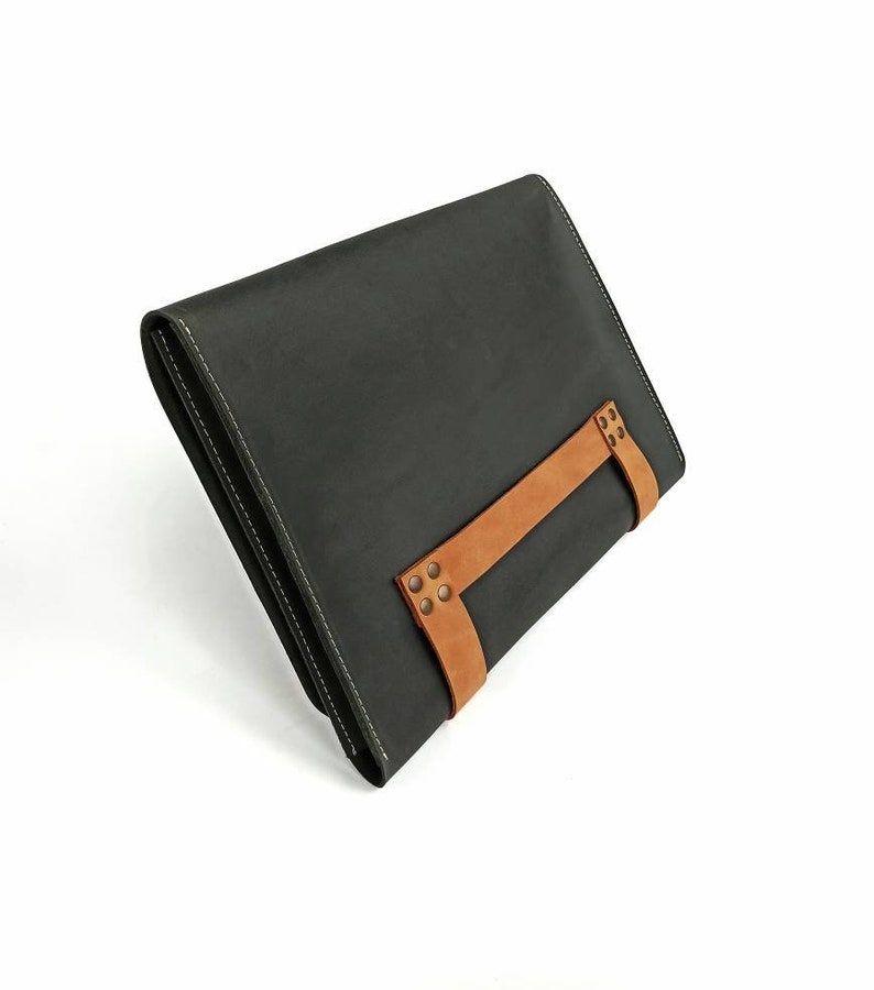 May include: A dark gray leather clutch with a brown leather strap and metal accents.