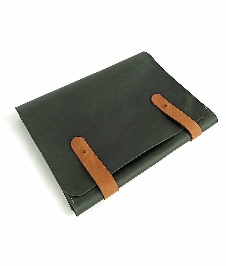 May include: A dark green leather laptop sleeve with two brown leather straps and metal buckles.
