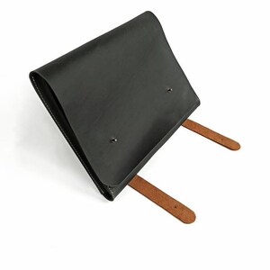 May include: A black leather envelope with two brown leather straps. The envelope has a flap that closes with a snap.