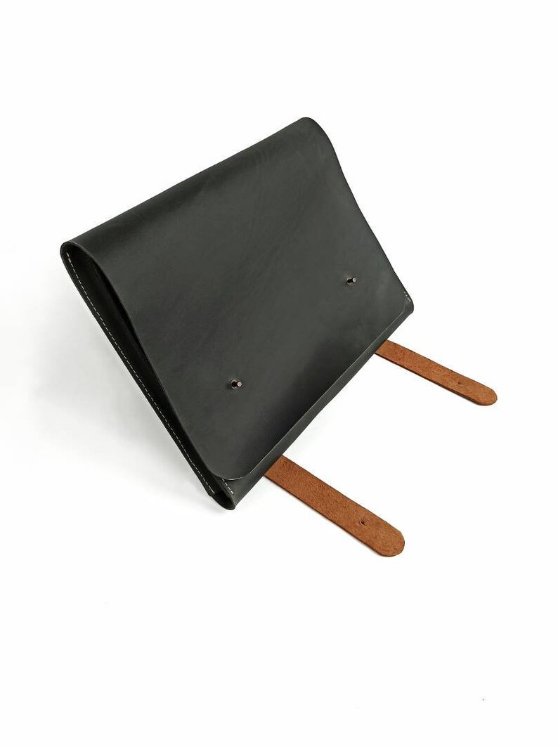 May include: A black leather envelope with two brown leather straps. The envelope has a flap that closes with a snap.