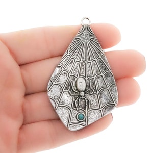 May include: Silver pendant charm featuring a spider in a web design with a turquoise stone in the center.