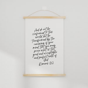 May include: A white canvas print with a black handwritten quote from the Bible, Romans 12:2, "And do not be conformed to this world, but be transformed by the renewing of your mind. That you may prove what is that good and acceptable and perfect will of God."
