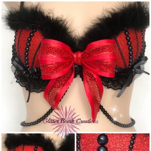 May include: A red and black lingerie top with a large red bow and black feather trim. The top is embellished with black beads and lace. The text "Valentines Pearls" is visible in the image.