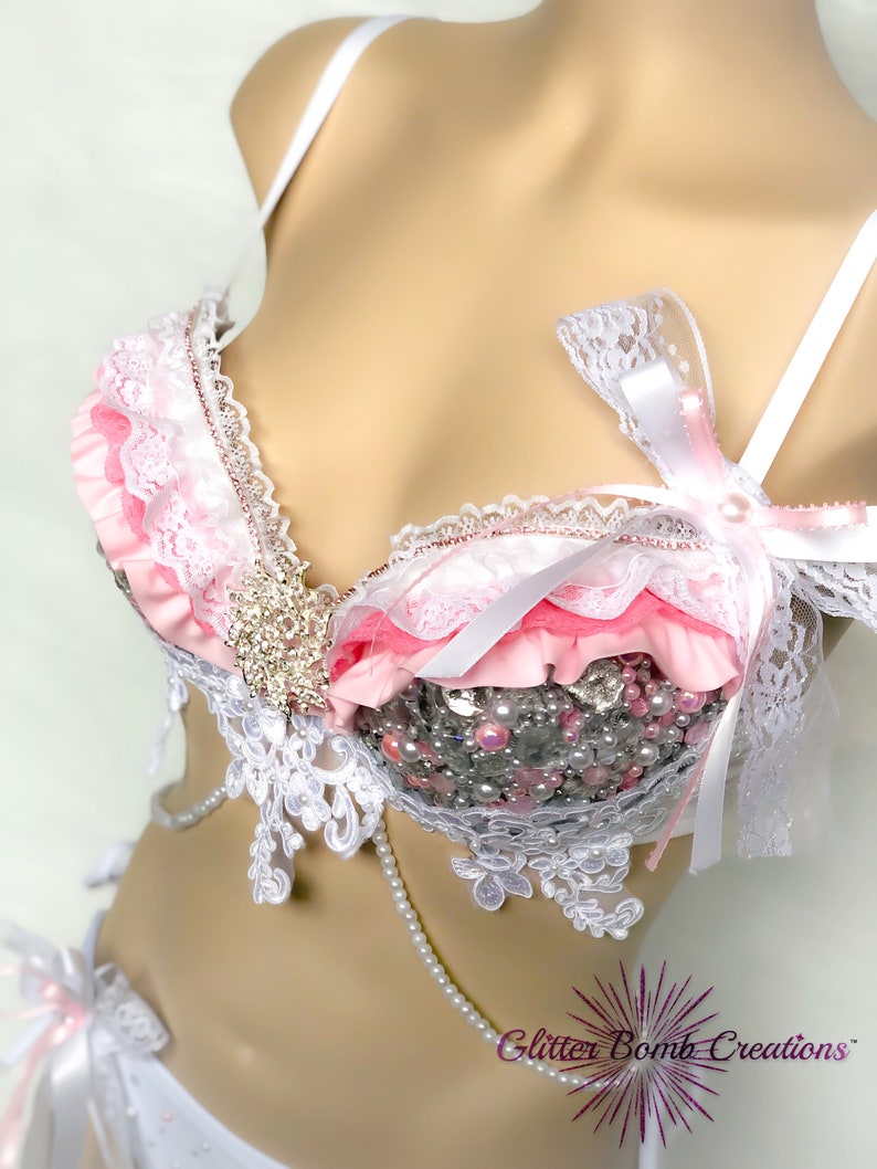 Op de afbeelding: Een roze en witte lingerie set met kant details en parel accenten. De bh heeft een roze ruche rand en een witte strik. De set is gemaakt door Glitter Bomb Creations.