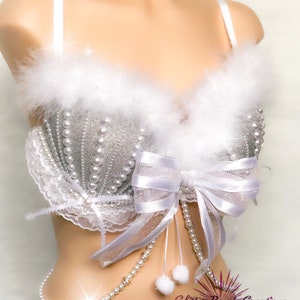 Pu&ograve; includere: Un reggiseno bianco e argento con un bordo di pelliccia bianca, un fiocco bianco e una catena di perle. Il reggiseno &egrave; in tessuto glitterato argento e perle bianche.