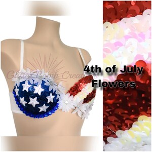 May include: A decorated bra featuring a blue sequined cup with white star appliqu&eacute;s and a red and white striped sequined cup. The garment is embellished with white fabric flowers along the top and center, and blue circular gems along the bottom edge.