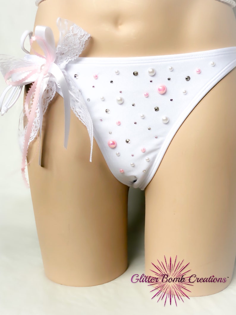 Op de afbeelding: Witte lingerie met een roze en witte kanten strik en parelversieringen. De lingerie is op een wit mannequin.