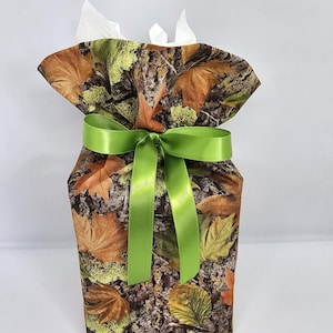 May include: A fabric tissue box cover with a camouflage pattern of brown, orange, and green leaves. The cover is tied with a bright green satin ribbon, and white tissues peek out from the top.