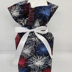 May include: A fabric gift bag with a festive firework pattern in red, white, and blue. The bag is tied with a white ribbon and contains white tissue paper, perfect for a patriotic celebration or gift-giving occasion.