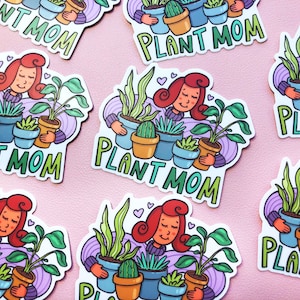 May include: A set of colorful stickers featuring a cartoon woman with red hair holding various potted plants. The stickers say "Plant Mom" in a whimsical font.