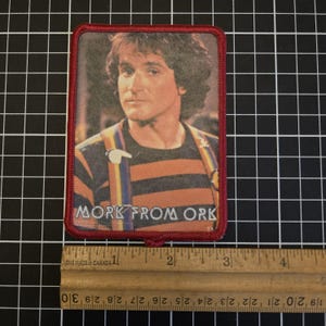 May include: Rectangular patch featuring a portrait of Robin Williams as Mork from the TV show Mork & Mindy. The patch has a red border and the text "MORK FROM ORK". The image shows Williams wearing a striped shirt and suspenders.