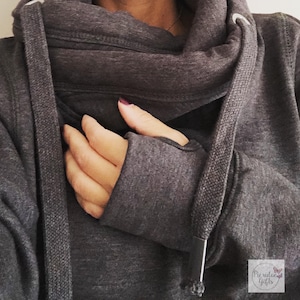 May include: Dark grey hoodie with a cowl neck and thumbhole cuffs. The hoodie features a drawstring and a small logo in the bottom right corner. The fabric appears to be a soft, medium-weight material.