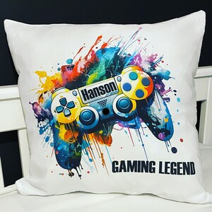 May include: White pillow with a colorful paint splatter design featuring a video game controller. The controller is blue, yellow, and black with the name "Hanson" printed on it. The text "GAMING LEGEND" is printed below the controller.