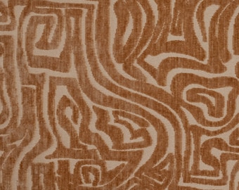 Op de afbeelding: Een textielstof met een gestructureerd, verhoogd patroon van onderling verbonden, kronkelende lijnen in een warme koperbruine kleur tegen een vlakke, lichtbeige achtergrond. Het ontwerp bestaat uit abstracte, doolhofachtige vormen en bochten.