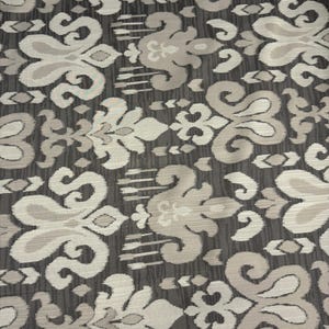May include: A fabric featuring a repeating damask-style pattern in light beige and cream tones set against a dark charcoal gray background. The design consists of symmetrical, stylized floral motifs with intricate, flowing curves.