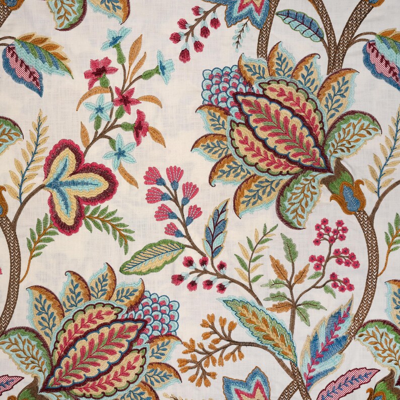 May include: A white fabric featuring an intricate, multi-colored floral embroidery pattern. The design includes large, stylized blossoms in shades of magenta, teal, gold, and green, connected by brown, textured, vine-like stems and small berries.