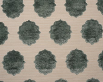 Op de afbeelding: Een textielstof met een herhalend patroon van donkergroenblauwe, geschulpte, wolkachtige vormen gerangschikt in een raster. De achtergrond is een lichtbeige, geweven materiaal met een zichtbare horizontale textuur over het gehele oppervlak.