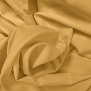 May include: A solid mustard yellow fabric with a smooth, matte texture. The material is draped in soft, flowing folds, creating deep shadows and highlights across the surface that emphasise the consistent colour and uniform weave of the textile.