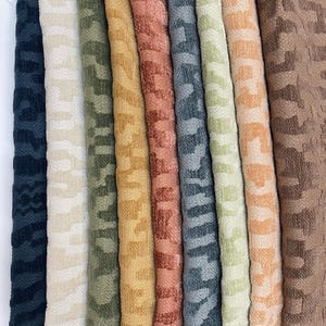 May include: A collection of nine folded fabric swatches arranged vertically, each featuring a consistent textured animal print pattern in distinct colors including black, cream, olive green, mustard yellow, terracotta, slate gray, sage, peach, and brown.