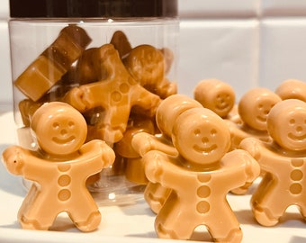Puede incluir: Un tarro transparente lleno de caramelos con forma de hombre de jengibre. Los caramelos son de color marrón claro y tienen una cara sonriente. Algunos de los caramelos están dispuestos en un plato blanco.