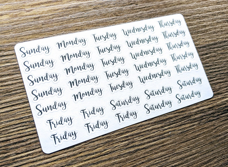 May include: A sheet of white stickers with black text. The stickers feature the days of the week: Sunday, Monday, Tuesday, Wednesday, Thursday, Friday, and Saturday.