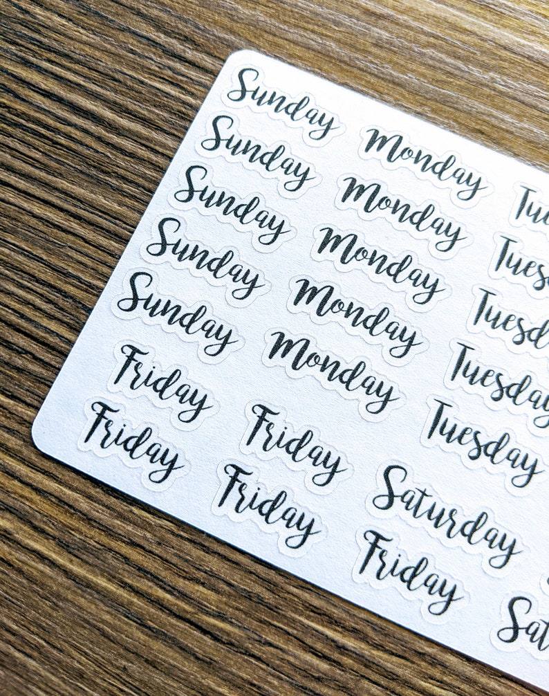 May include: A sheet of clear stickers with the days of the week written in black cursive. The stickers are arranged in rows and columns, with each day of the week repeated multiple times.