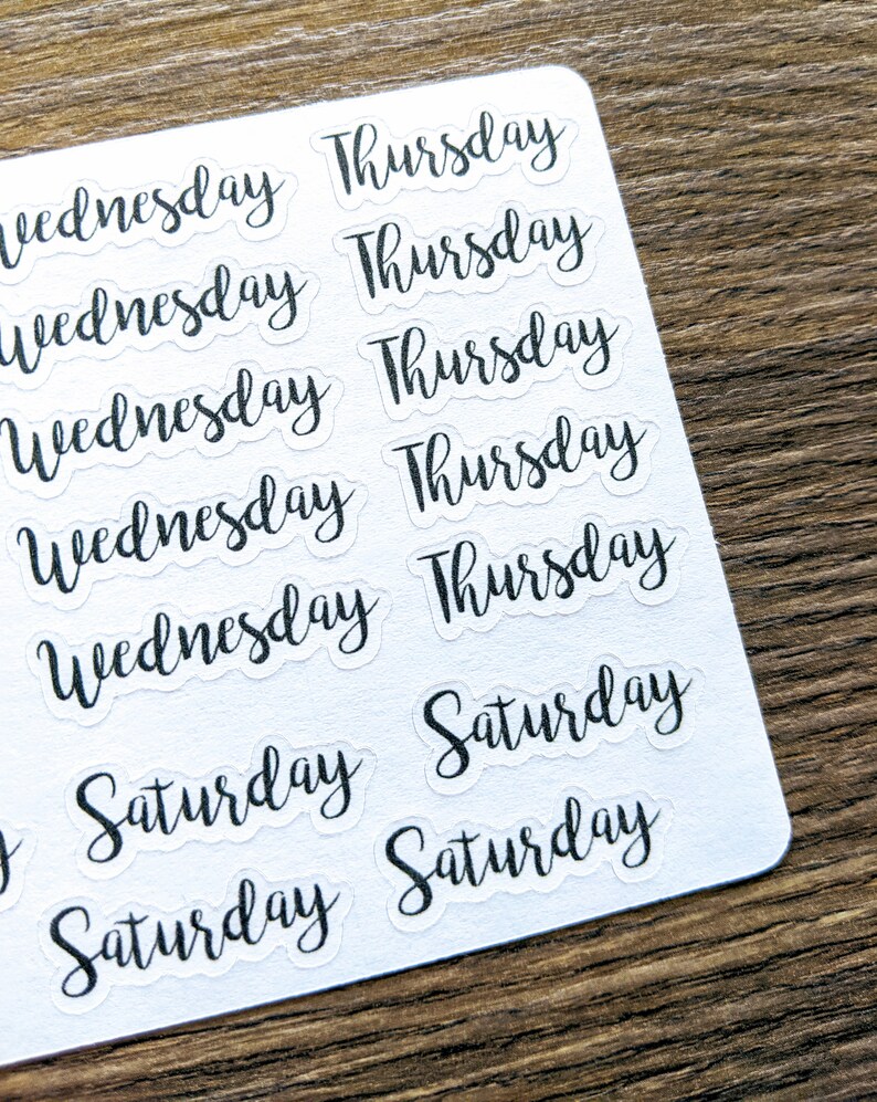 May include: A sheet of clear stickers with black lettering. The stickers feature the words "Wednesday", "Thursday", and "Saturday" repeated multiple times.