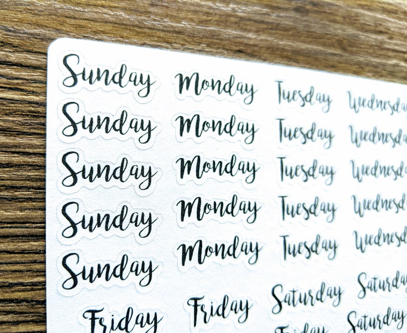 May include: A sheet of clear stickers with the days of the week written in black cursive lettering. The days of the week are Sunday, Monday, Tuesday, Wednesday, Thursday, Friday, and Saturday.