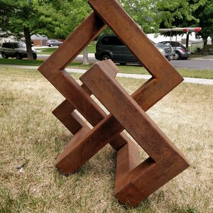 May include: A rusty metal sculpture in the shape of a cube with intersecting lines. The sculpture is standing on a grassy lawn.