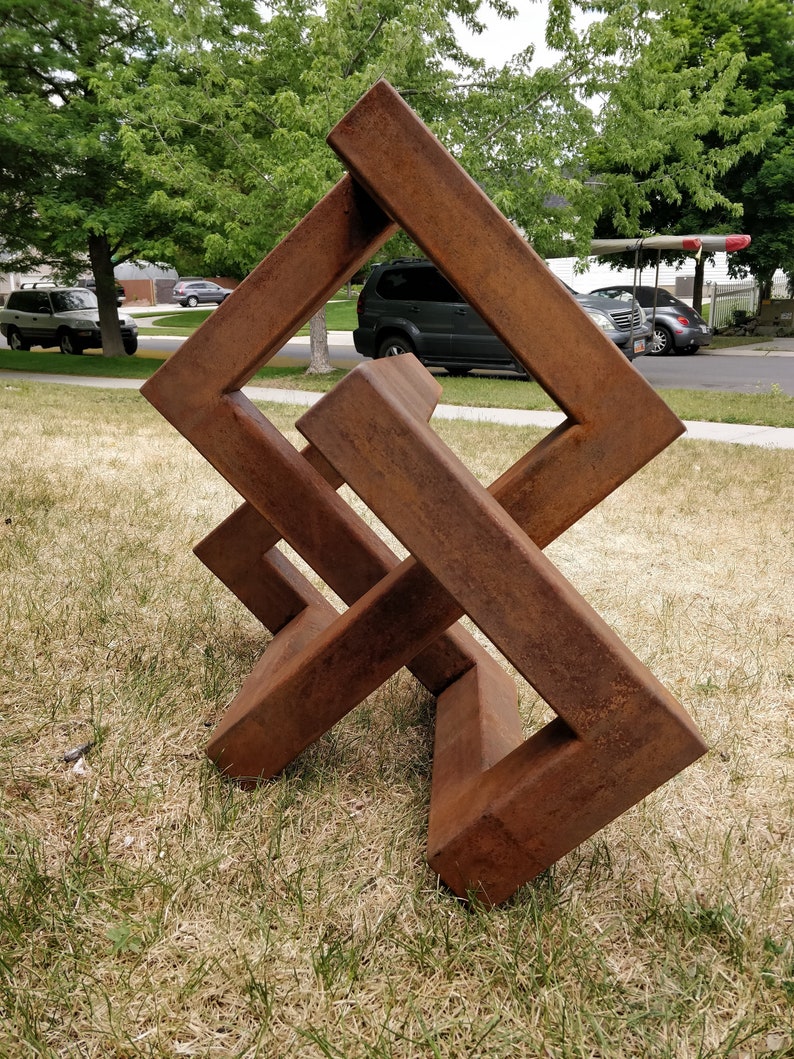 May include: A rusty metal sculpture in the shape of a cube with intersecting lines. The sculpture is standing on a grassy lawn.