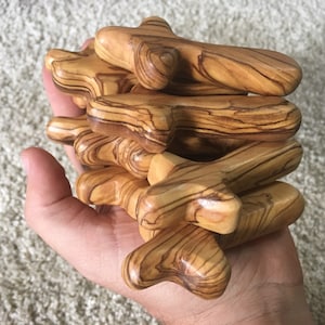 Puede incluir: Una pila de pequeñas cruces de madera de olivo. Las cruces tienen un color marrón claro natural con patrones de grano marrón oscuro.