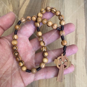 May include: A wooden rosary with brown beads and a Celtic cross pendant. The beads are made of olive wood and have a natural wood grain.