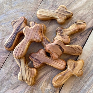 Puede incluir: Un grupo de siete pequeñas cruces de madera de olivo. Las cruces son de diferentes formas y tamaños, pero todas están hechas en el mismo estilo. Las cruces son de color marrón claro con vetas marrones oscuras.