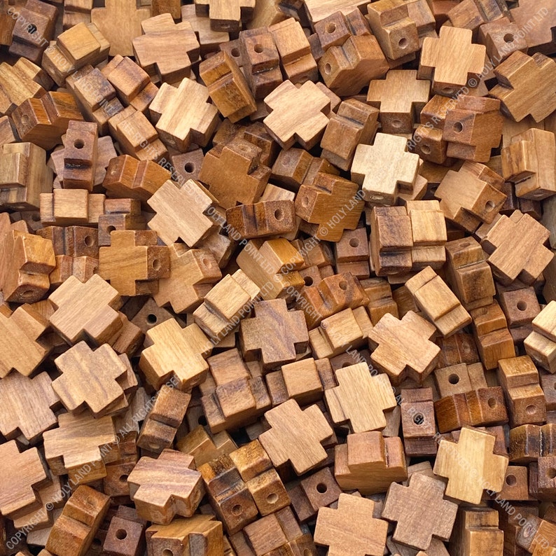 Pu&ograve; includere: Un'immagine ravvicinata di un mucchio di piccole perline di legno a forma di croce. Le perline sono di colore marrone chiaro e hanno una finitura liscia e lucida.