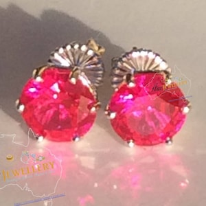 May include: A pair of silver stud earrings with a bright pink round gemstone in the center of each earring.