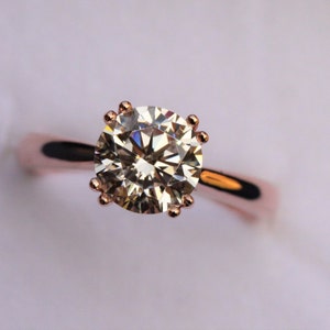 May include: A rose gold engagement ring with a large, round, clear diamond.